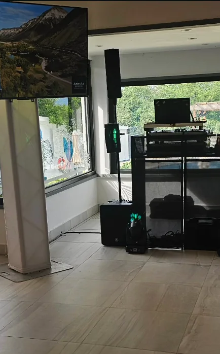 Montaje de DJ en un salón con vista, bocina en altura, moving head y televisor