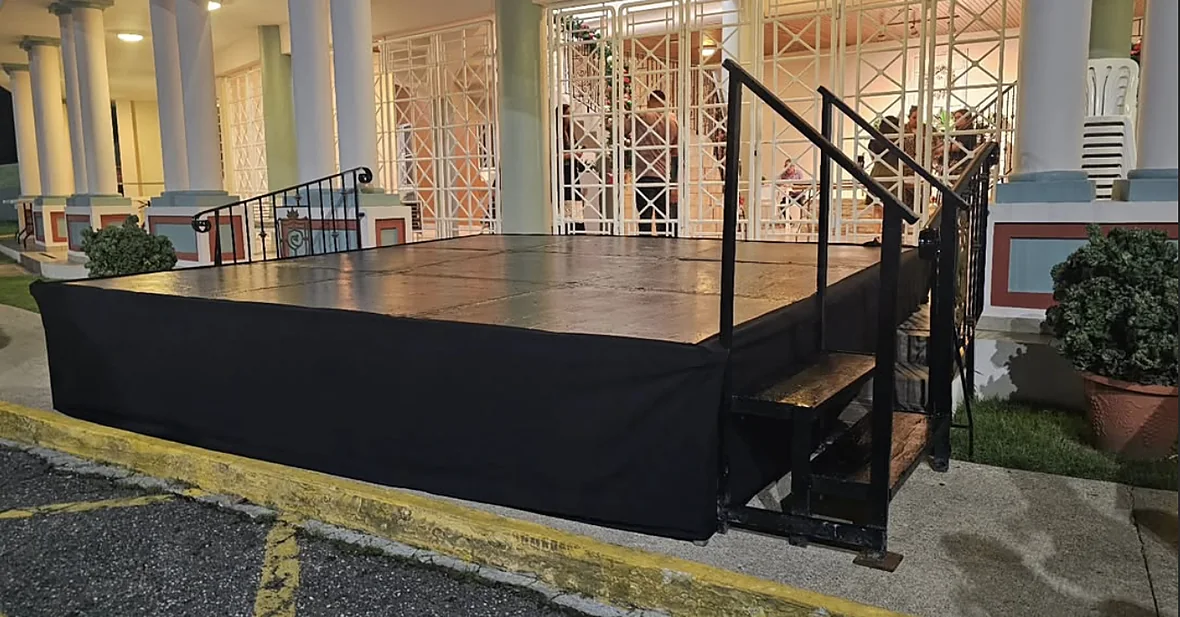 Tarima con faldón negro y escalera montada de noche frente a un edificio con columnas